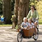 Young woman cycles with her cargo bike with children through the Vondelpark in Amsterdam